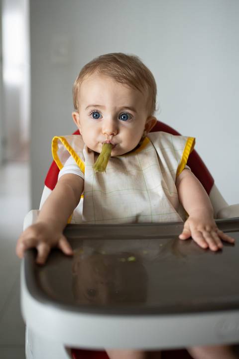 Bebê sentada na cadeira de alimentação com uma vagem na boca; fazendo biquinho; Joao-Francisco-Fotografia; Familia; Niteroi; Rio de Janeiro; Acompanhamento; life-style;'