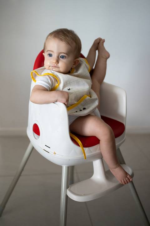 Bebê sentada na cadeira de alimentação segurando a perna esquerda para o alto; Joao-Francisco-Fotografia; Familia; Niteroi; Rio de Janeiro; Acompanhamento; life-style;'