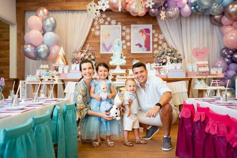 Festa infantil de aniversário de menina de 4 anos com o tema Frozen; princesa Elsa; princesa Anna; vestido azul; retrato da família; pais agachados na altura dos filhos sorrindo para a foto; quintal de contos; niteroi; Rio de Janeiro; fotografo de familia'