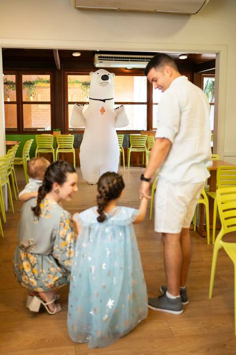 Festa infantil de aniversário de menina de 4 anos com o tema Frozen; princesa Elsa; princesa Anna; vestido azul; família de costas desfocada observando personagem urso polar inflável; quintal de contos; niteroi; Rio de Janeiro; fotografo de familia'