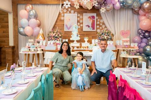 Festa infantil de aniversário de menina de 4 anos com o tema Frozen; princesa Elsa; princesa Anna; vestido azul; retrato dos avós e neta abaixados em frente a mesa do bolo; quintal de contos; niteroi; Rio de Janeiro; fotografo de familia'