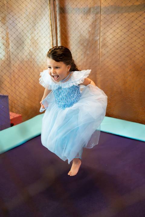 Festa infantil de aniversário de menina de 4 anos com o tema Frozen; princesa Elsa; princesa Anna; menina de vestido azul pulando na cama elástica'