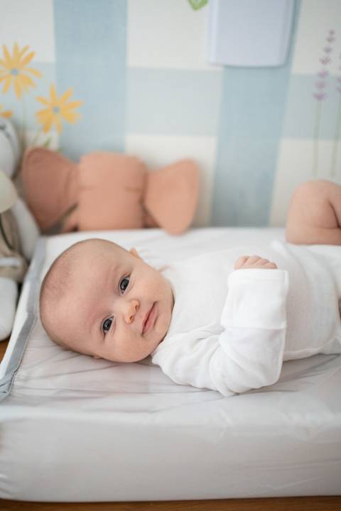 Bebê menina de 3 meses deitada no trocador, carequinha, de body branco, olhando para a câmera; Joao-Francisco-Fotografia; Familia; Niteroi; Rio de Janeiro; Acompanhamento; life-style;'