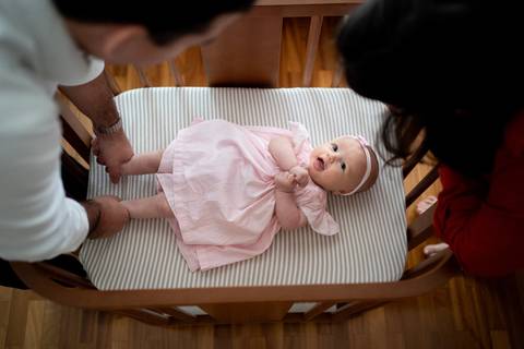 Bebê menina de 3 meses deitada no berço olhando para o alto; foto tirada de cima pra baixo; berço de madeira; Pais observando a bebê; Joao-Francisco-Fotografia; Familia; Niteroi; Rio de Janeiro; Acompanhamento; life-style;'