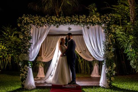 Fotografia de noivos clássica em casamento rústico embaixo de gazebo florido com cortina branca'