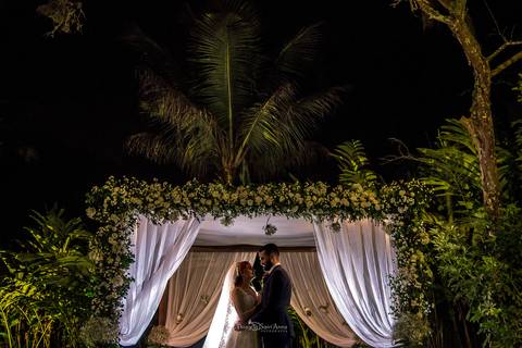 Fotografia de noivos clássica em casamento rústico embaixo de gazebo florido com cortina branca'