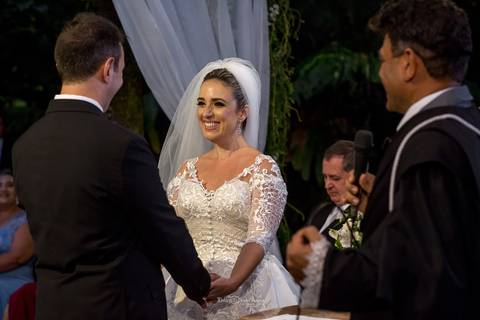 Noiva sorri segurando as mãos do noivo'