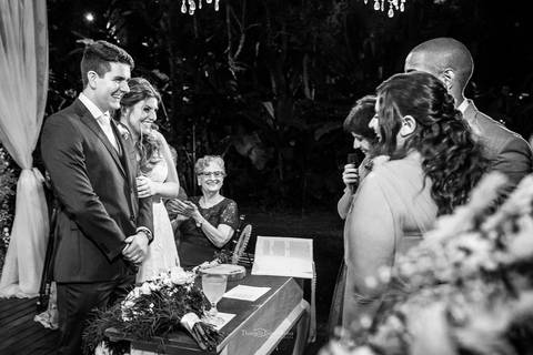 noivos sorriem no altar familiares observam preto e branco'