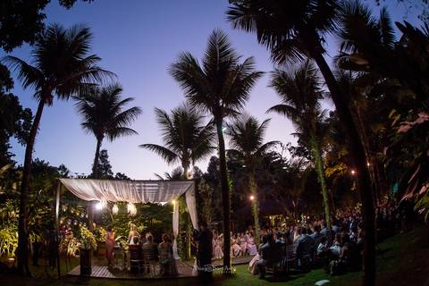 local aberto anoitecer palmeiras tenda de madeira com tecidos brancos altar convidados '
