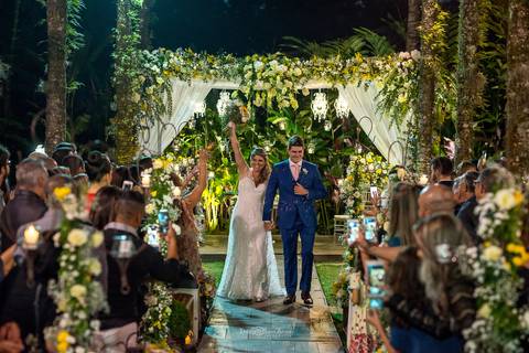 saída dos noivos convidados observam de pé decoração vegetal flores brancas e amarelas '