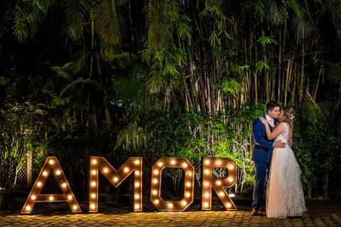 noivos se beijam ao lado de de letreiro luminoso decoração vegetal '