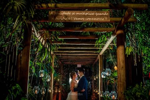 noivos se abraçam em caminho de madeira com vegetação luminárias '