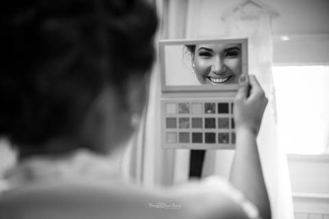 noiva sorri pelo reflexo do espelho de uma paleta de maquiagens '