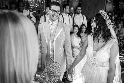 noivos se observam sorrindo padrinhos ao fundo preto e branco'