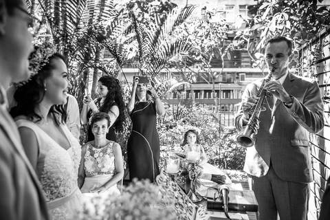 músico toca trompete durante a cerimônia noivos observam preto e branco'
