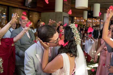 beijo dos noivos sob queda de pétalas cor de rosa padrinhos observam sorrindo '