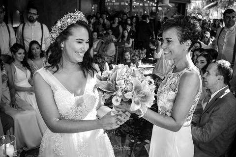 noiva observa sua buque sorrindo com sua madrinha padrinhos e convidados ao fundo preto e branco'