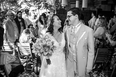 noivos se olham sorrindo convidados ao fundo preto e branco'