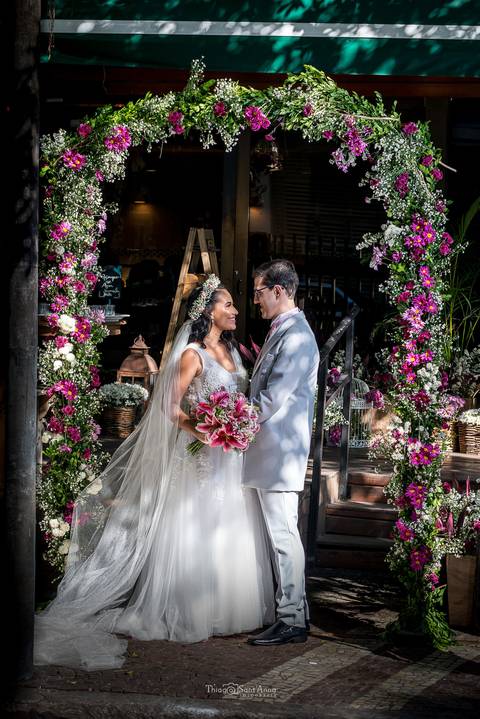 noivos se observam sorrindo abraçados decoração flores em tons de rosa vestido buque'