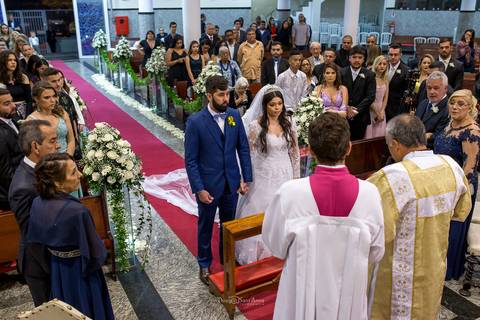 noivos no altar tapete vermelho convidados observam de pé pais dos noivos e padre realiza a cerimônia'