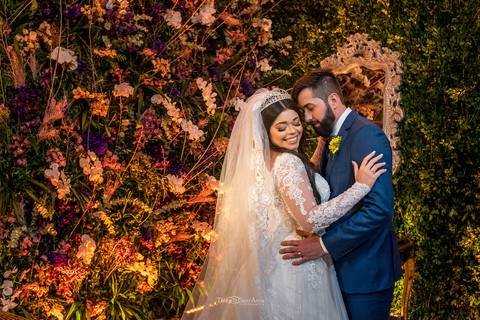 noivos se abraçam noiva sorri parede decorada vegetação flores '