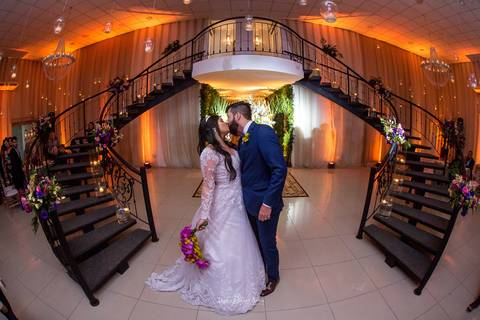 noivos se beijam entre escadas decoradas com flores lustres '