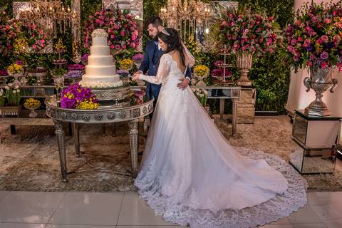 noivos cortam o bolo noiva grinalda buque rosa e amarelo decoração paredes com vegetação flores em tons de rosa '