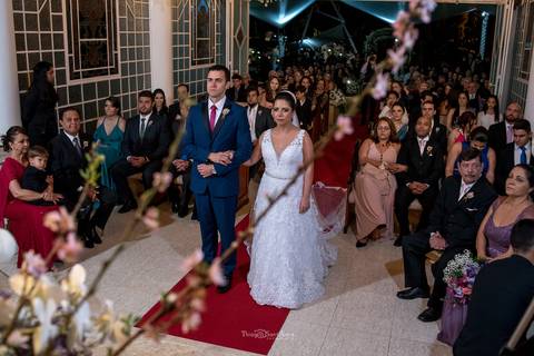 noivos tapete vermelho noiva vestido véu noivo terno azul gravata vermelha padrinhos e convidados observam'
