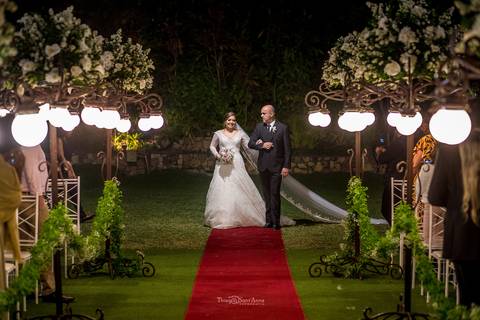 entrada da noiva com seu pai vestido véu buque tapete vermelho vegetação flores brancas postes luminárias '