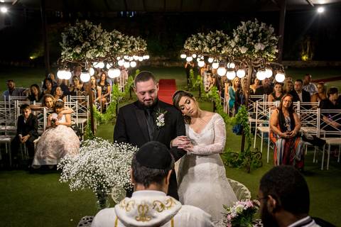 noivos no altar padre realiza cerimônia arranjo flores brancas decoração postes luminárias flores brancas'
