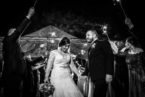 saída dos noivos de mãos dadas padrinhos levantam bastões luminosos preto e branco'