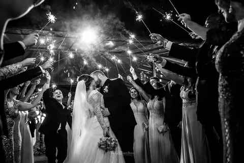 beijo dos noivos em meio a padrinhos que levantam bastões luminosos preto e e branco'