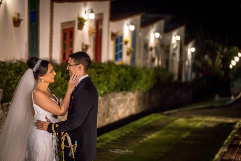noiva toca o rosto do noivo que pega em sua cintura rua de paralelo ao lado de casas rústicas portas e janelas coloridas '