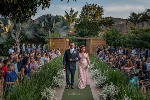 entrada noivo e sua mãe decoração vegetal flores brancas árvores palmeiras convidados observam '