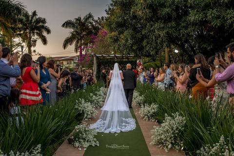 entrada da noiva com seu pai convidados observam de pé vegetação flores brancas'