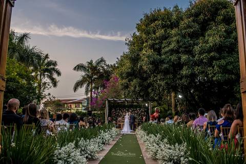 noivos no altar vegetação árvores flores brancas convidados observam sentados'
