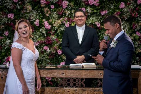 noiva sorri noivo lê seus votos padre sorri parede flores tons de rosa'