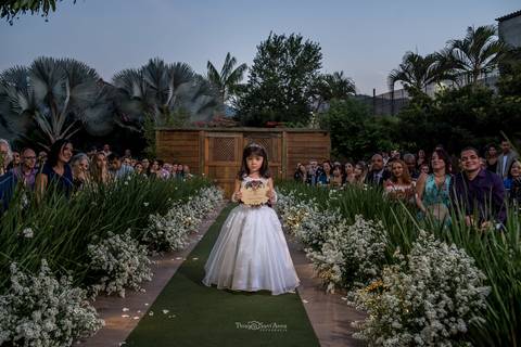 dama de honra leva alianças convidados ao fundo vegetação flores brancas'