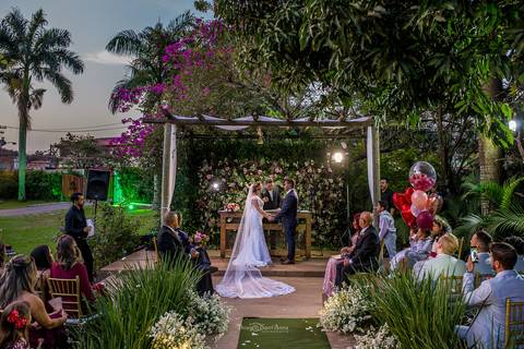 noivos no altar tenda madeira tecido branco convidados observam vegetação balões flores '