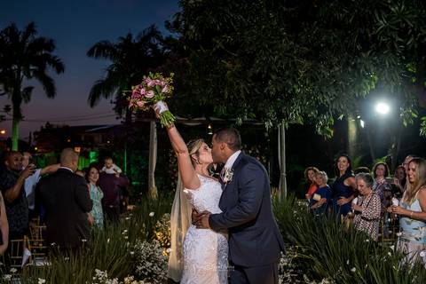 beijo dos noivos noiva levanta buque convidados ao fundo'