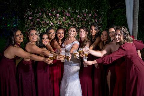 noiva brinda com madrinhas usam vestido bordô parede flores tons de rosa ao fundo'