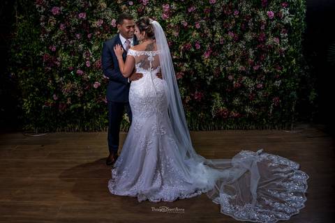 noivos se abraçam noiva vestido véu parede flores tons de rosa ao fundo'