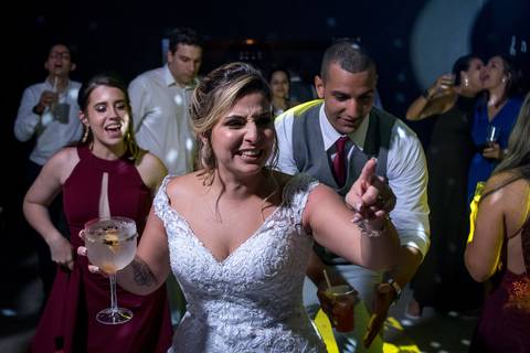 noiva sorri aponta e dança padrinhos e convidados dançam ao fundo'