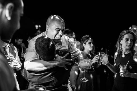 padrinho abraça o noivo convidados ao fundo preto e branco'