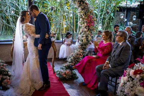 beijo dos noivos tapete vermelho arco de flores tons de rosa '