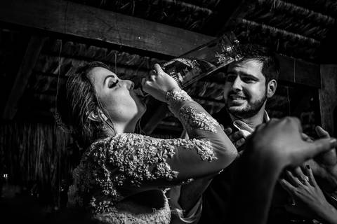 noiva toma bebida direto da garrafa noivo observa preto e branco'