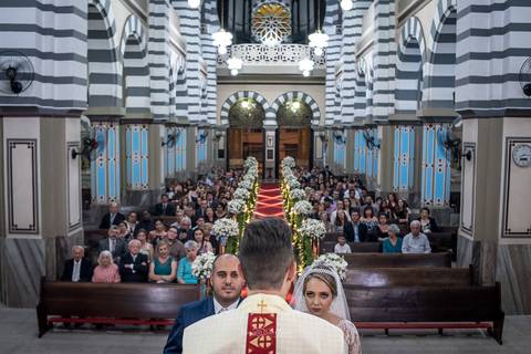 noivos no altar junto ao padre igreja convidados ao fundo '