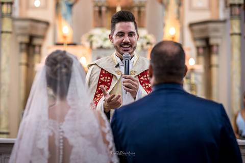 padre sorri falando aos noivos igreja altar'
