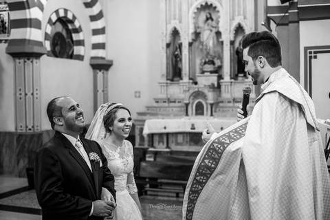 noivos sorrindo junto ao padre no altar preto e branco'