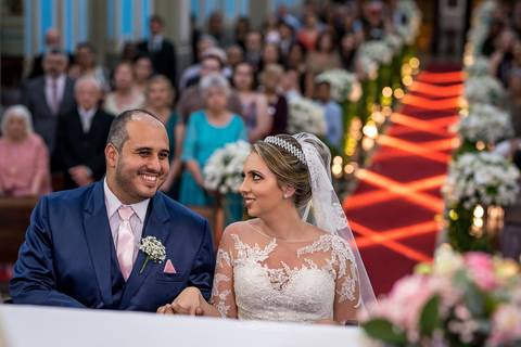 noivos sorrindo no altar convidados ao fundo decoração flores brancas e tons de rosa '